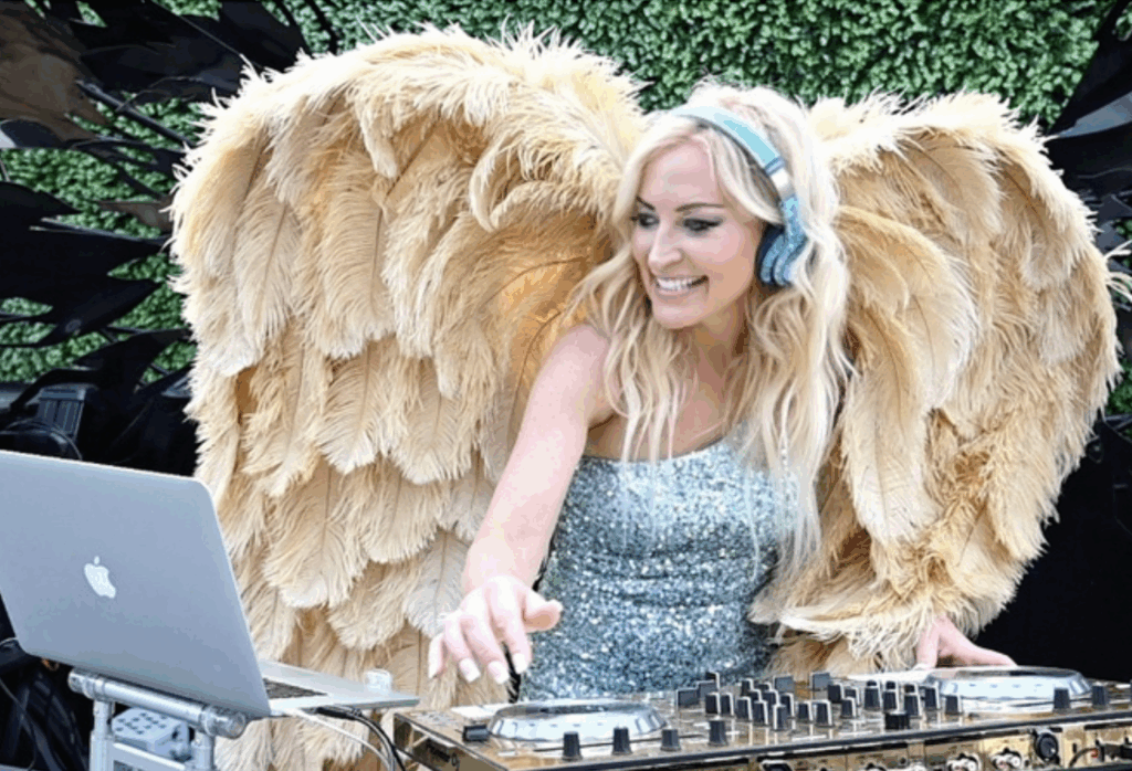 DeeJay Shelly wearing gold wings and a turquoise dress while DJing with her Pioneer gold controller.