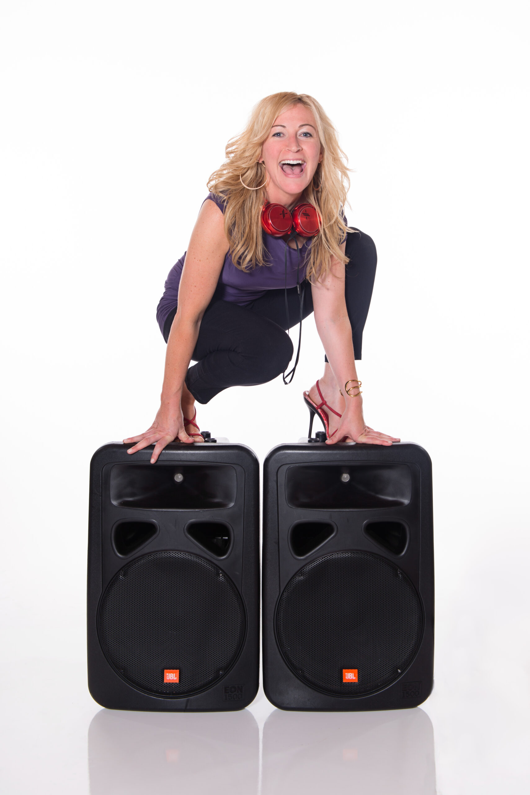 Female DJ DeeJay Shelly standing on JBL speakers wearing red headphones and red heels