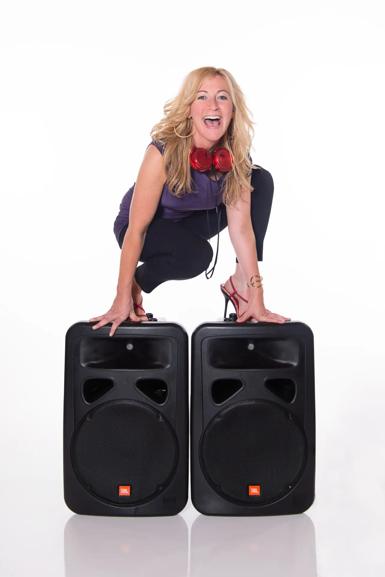 Female DJ DeeJay Shelly standing on JBL speakers wearing red headphones and red heels